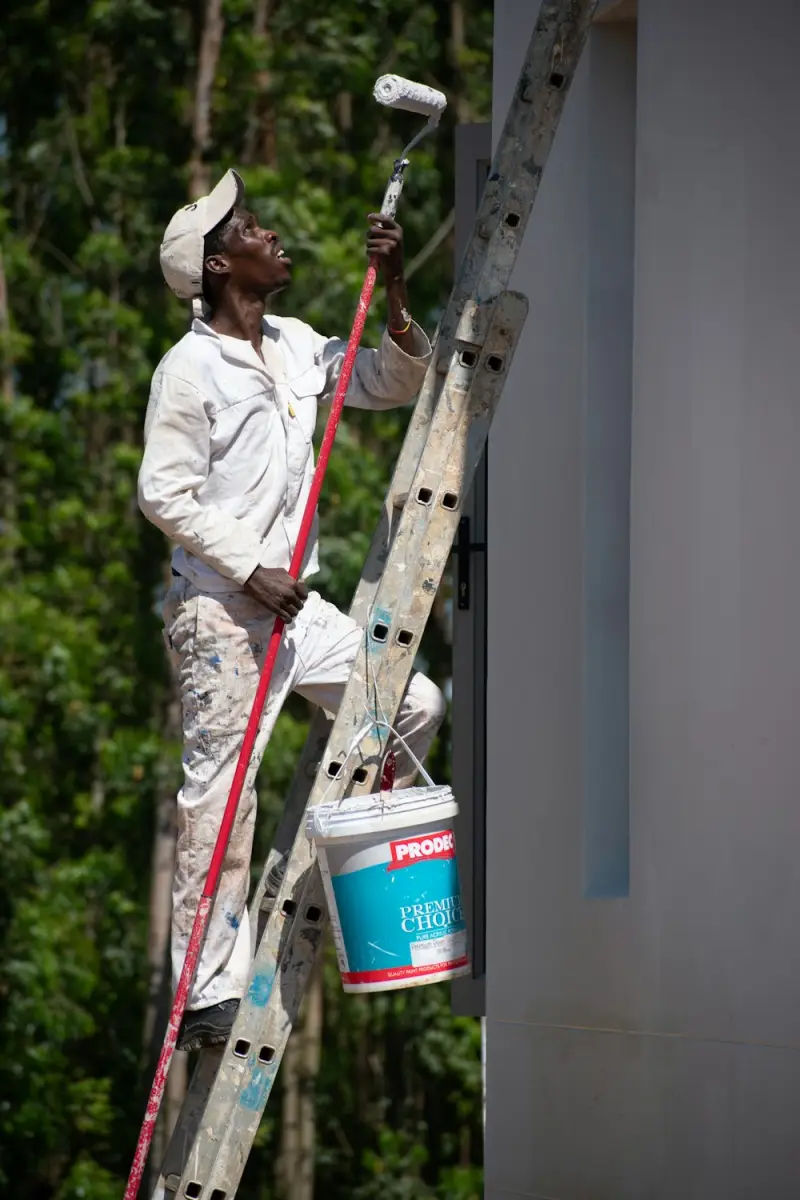 A painter on a ladder rolling paint onto an outside wall.